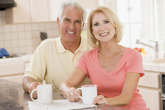 Older man and woman smiling for the camera at the kitchen table
