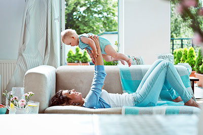 woman laying on sofa playing with baby in her arms