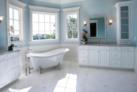 A clean bathroom with blue walls, white trim, white cabinets, and a white bathtub
