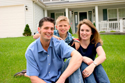 A woman, man, and young boy posing on the lawn in front of a home