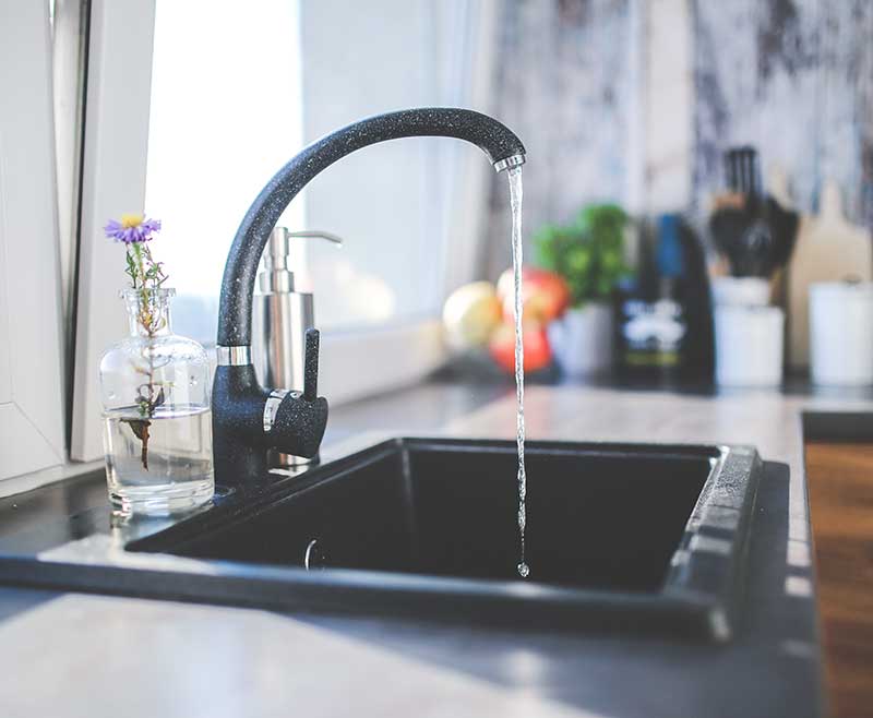 A kitchen sink faucet pouring water into the sink basin