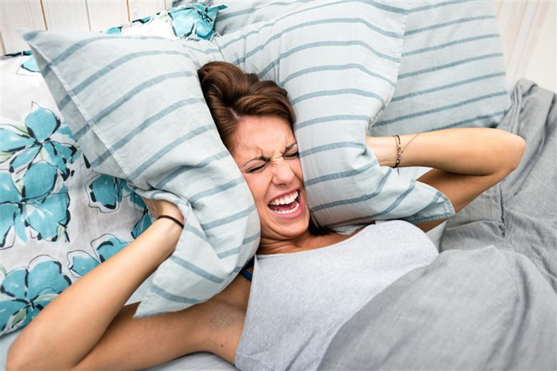 woman covering ears with a pillow because of loud noise