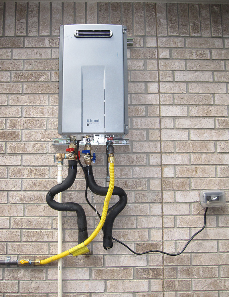 Silver tankless water heater affixed to a brick wall