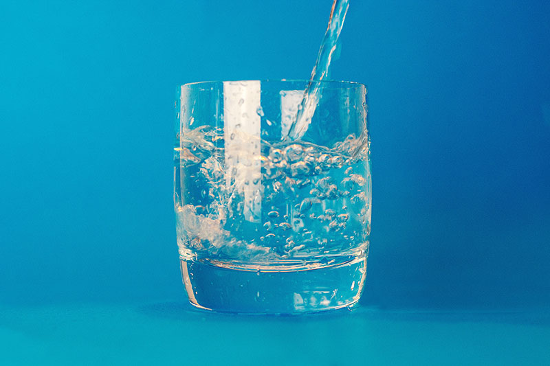 closeup of water pouring into a cup with a blue background