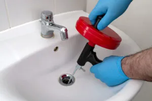 plumber using drain snake on bathroom sink drain