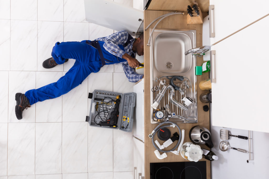 plumber under cabinet fixing sink