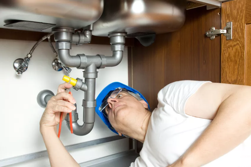 plumbing technician in white shirt adjusting pipes under cabinet