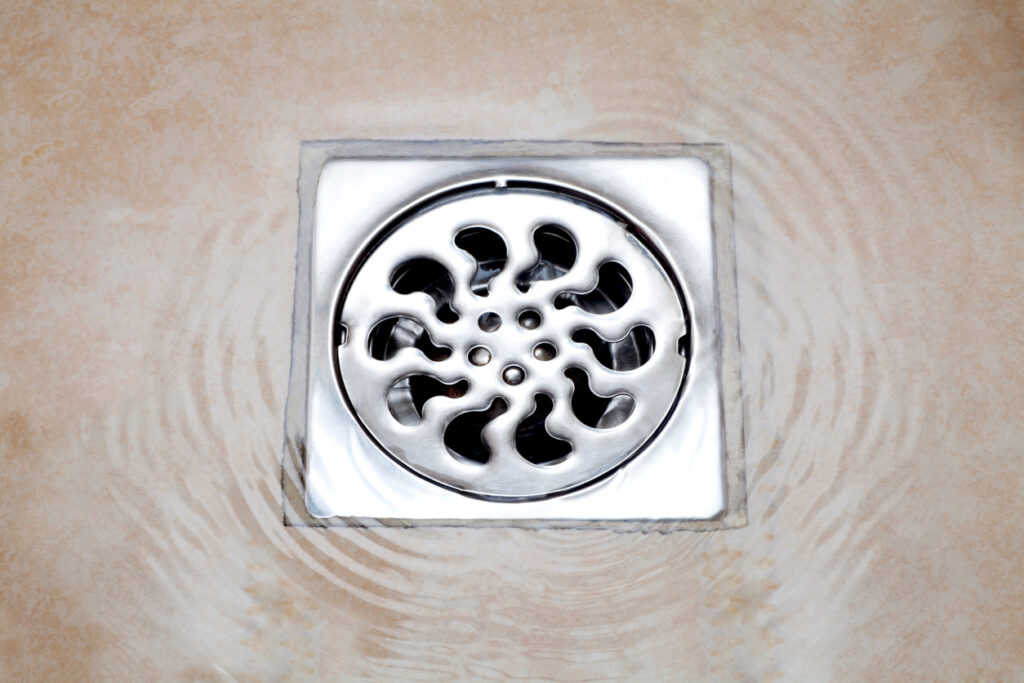 Water flowing over into metal drain on the tiled floor of a shower.